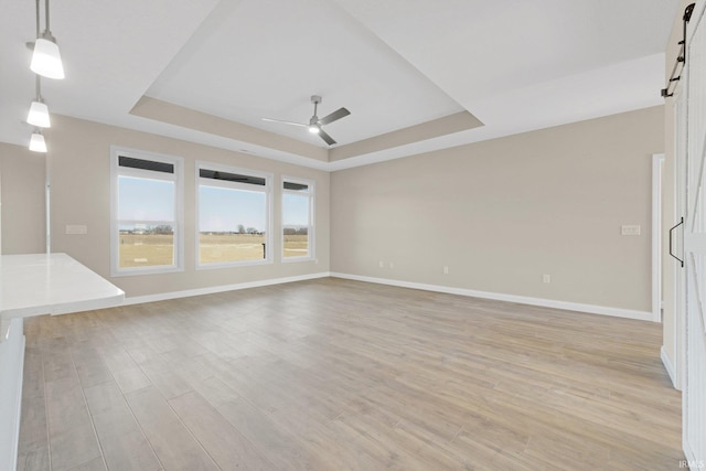 6711 W Division Line Rd, Delphi, IN 46923 - unfurnished living room featuring ceiling fan, a barn door, light wood-style flooring, baseboards, and a tray ceiling