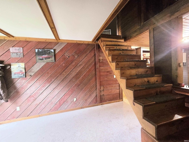 stairway featuring beamed ceiling, carpet floors, and wood walls