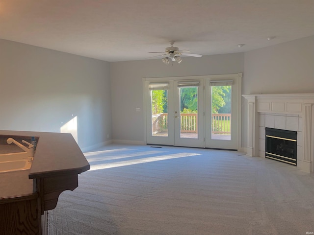 unfurnished living room featuring ceiling fan, a tiled fireplace, sink, and light carpet