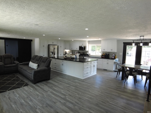 kitchen with appliances with stainless steel finishes, pendant lighting, white cabinets, decorative backsplash, and hardwood / wood-style flooring