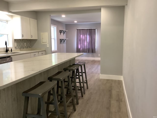 kitchen featuring white cabinetry, sink, a kitchen bar, decorative backsplash, and light wood-type flooring