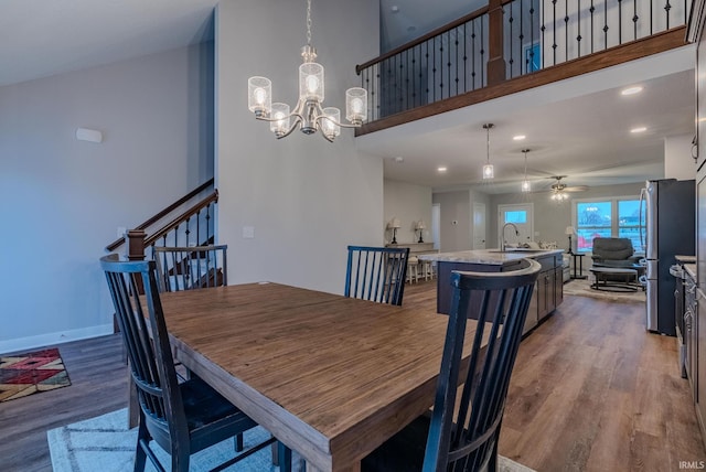 dining space featuring a towering ceiling, baseboards, recessed lighting, ceiling fan with notable chandelier, and wood finished floors
