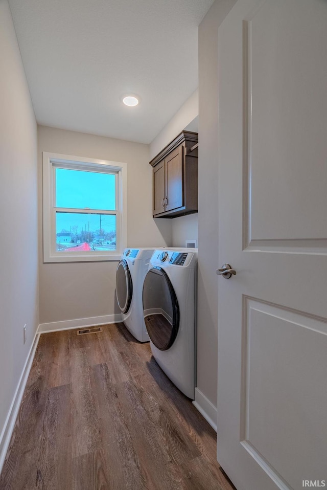 clothes washing area featuring dark wood finished floors, visible vents, washing machine and clothes dryer, baseboards, and cabinet space