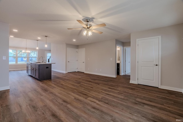 kitchen with dark wood-type flooring, a center island with sink, ceiling fan with notable chandelier, sink, and decorative light fixtures