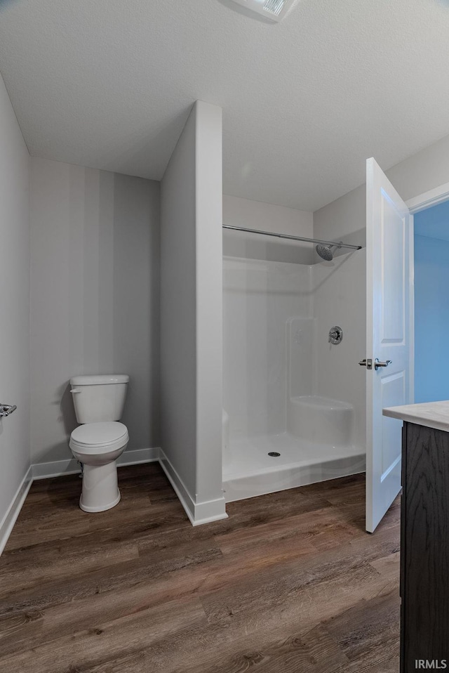 bathroom with a textured ceiling, toilet, wood-type flooring, and walk in shower