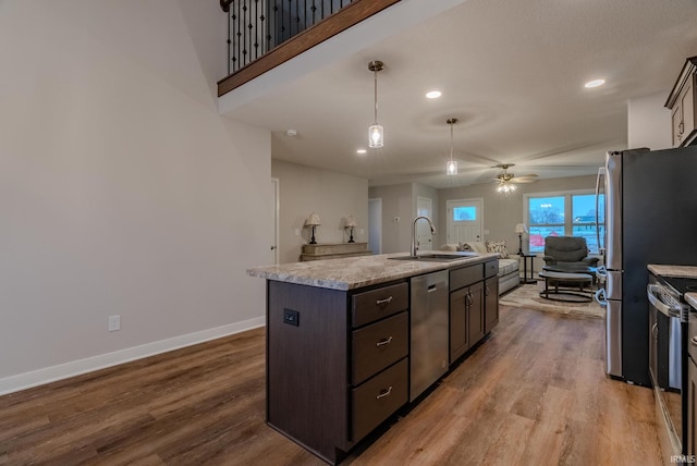 kitchen featuring stainless steel appliances, dark brown cabinets, a sink, a center island with sink, and open floor plan