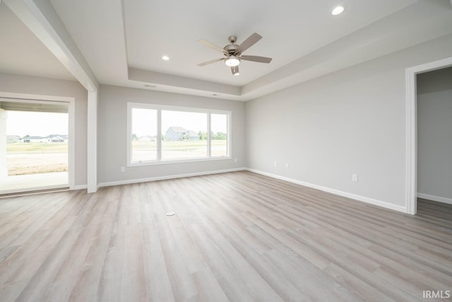 interior space featuring ceiling fan, light wood-type flooring, and a tray ceiling