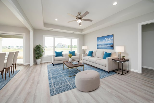 living room featuring light hardwood / wood-style floors, a raised ceiling, and ceiling fan