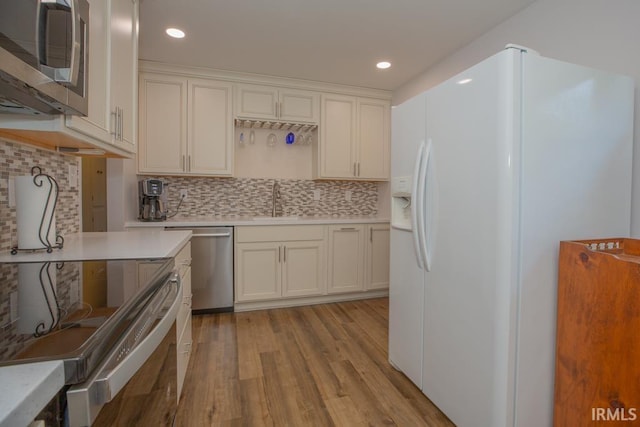 kitchen featuring white cabinets, appliances with stainless steel finishes, tasteful backsplash, light hardwood / wood-style floors, and sink