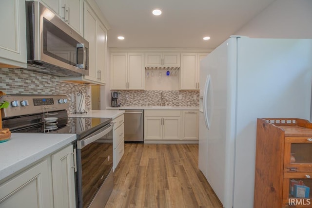 kitchen featuring white cabinets, backsplash, appliances with stainless steel finishes, and light hardwood / wood-style flooring