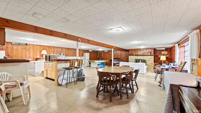 dining space with beam ceiling, washer / clothes dryer, a stone fireplace, and wooden walls