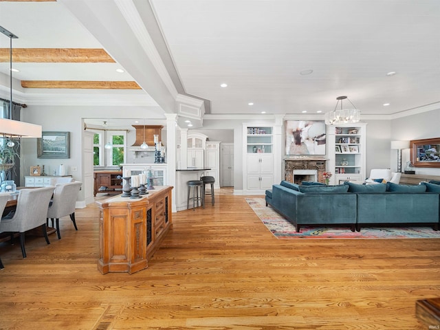 living room with light wood-type flooring, built in shelves, crown molding, beamed ceiling, and a stone fireplace