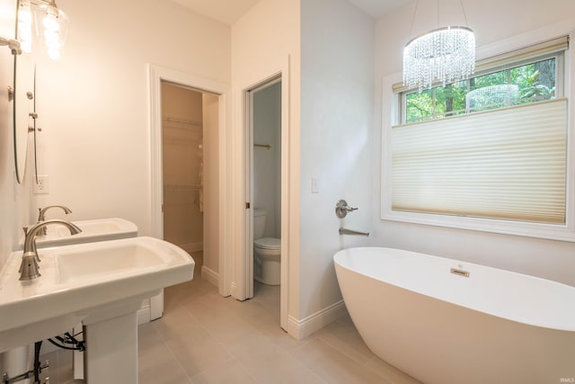 bathroom with tile patterned flooring, a chandelier, a bathing tub, toilet, and sink