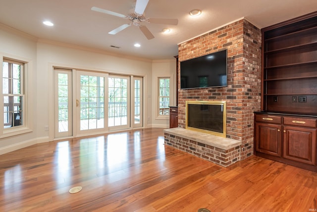 unfurnished living room featuring ornamental molding, a brick fireplace, ceiling fan, and light wood-type flooring