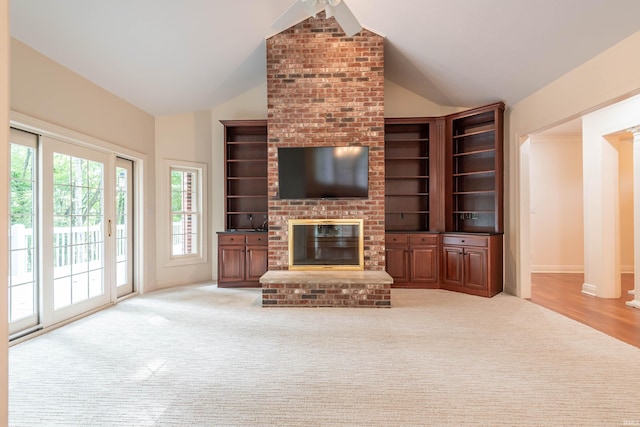 living room with lofted ceiling, light hardwood / wood-style flooring, built in shelves, a brick fireplace, and brick wall