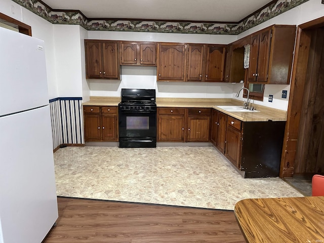 kitchen with black range with gas stovetop, sink, light hardwood / wood-style flooring, white fridge, and dark brown cabinetry