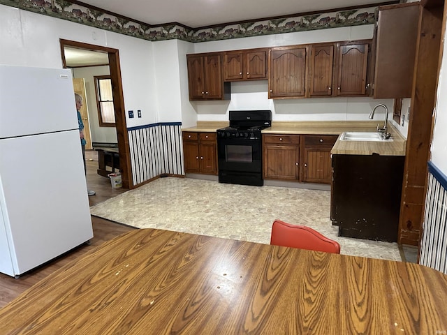 kitchen with sink, black gas stove, white fridge, hardwood / wood-style floors, and dark brown cabinets