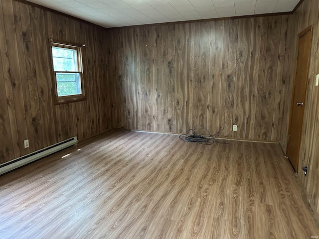 spare room with light hardwood / wood-style floors, baseboard heating, and wooden walls