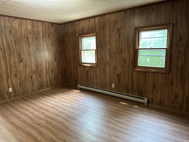 unfurnished room with wood walls, a baseboard radiator, and light wood-type flooring