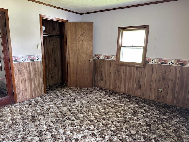 unfurnished bedroom with carpet, a closet, crown molding, and wood walls