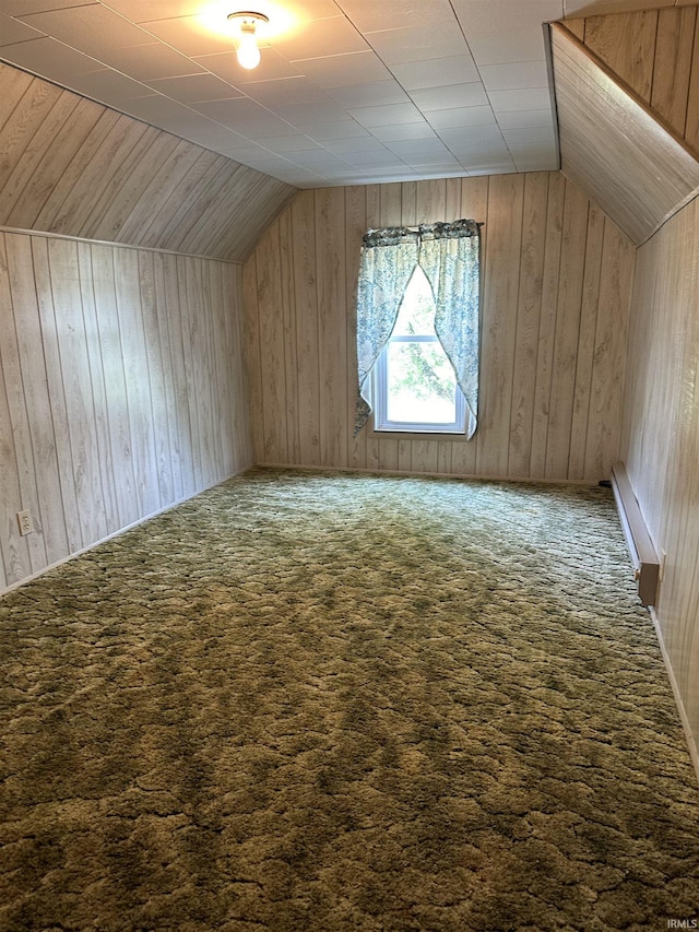 additional living space with dark colored carpet, vaulted ceiling, and wood walls