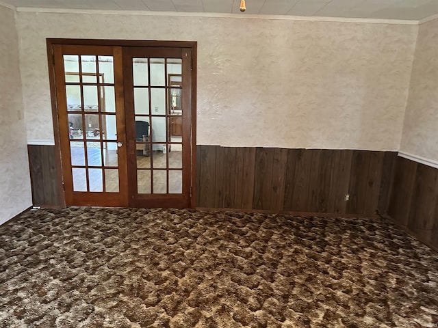 carpeted empty room with wood walls, crown molding, and french doors