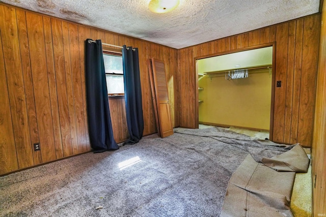 empty room featuring carpet floors, a textured ceiling, and wooden walls