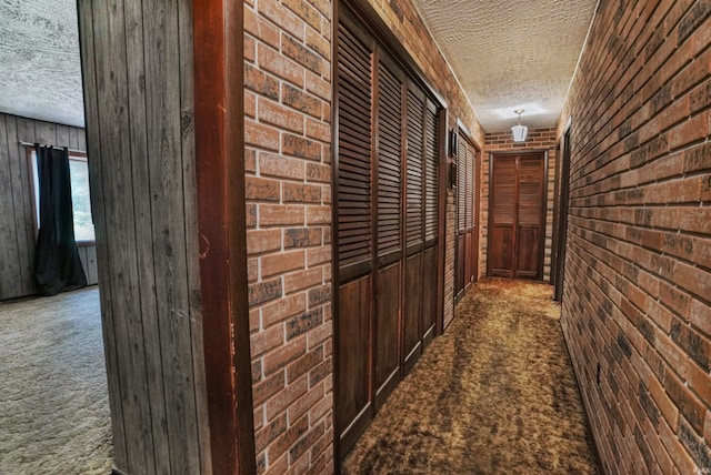 corridor featuring wooden walls, dark colored carpet, brick wall, and a textured ceiling