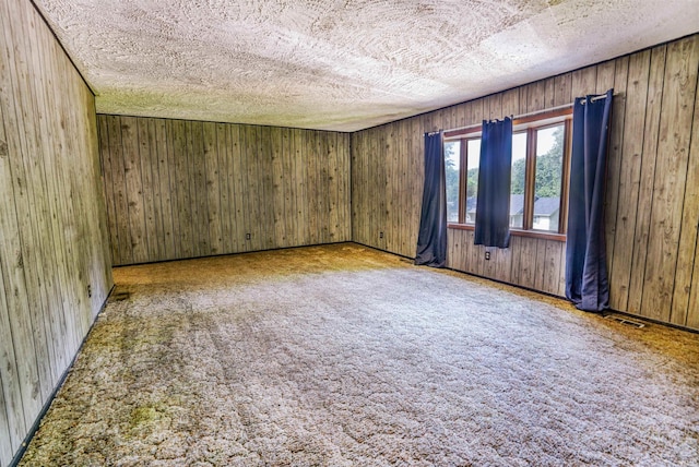 empty room with carpet, wooden walls, and a textured ceiling