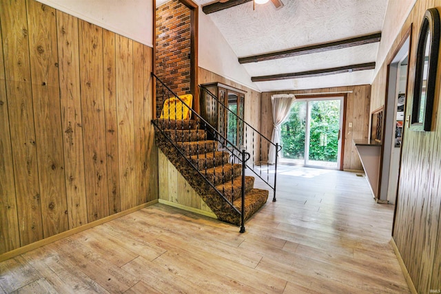 stairway with light hardwood / wood-style flooring, a textured ceiling, ceiling fan, brick wall, and lofted ceiling with beams