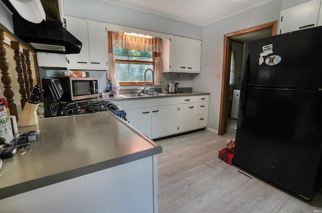 kitchen with light wood finished floors, under cabinet range hood, freestanding refrigerator, white cabinets, and a sink