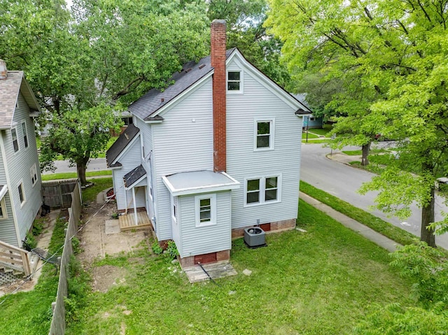 rear view of house with central AC and a lawn