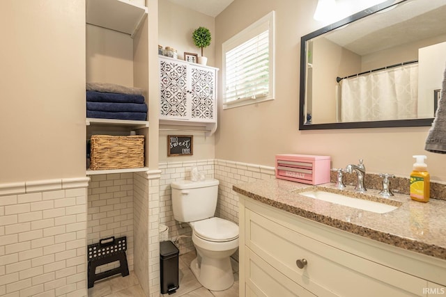 bathroom with toilet, tile patterned flooring, tile walls, vanity, and curtained shower