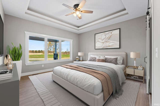 bedroom featuring light wood-style floors, a ceiling fan, a raised ceiling, and baseboards