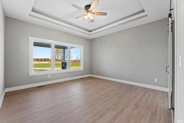 unfurnished room featuring ceiling fan, visible vents, a raised ceiling, baseboards, and light wood finished floors