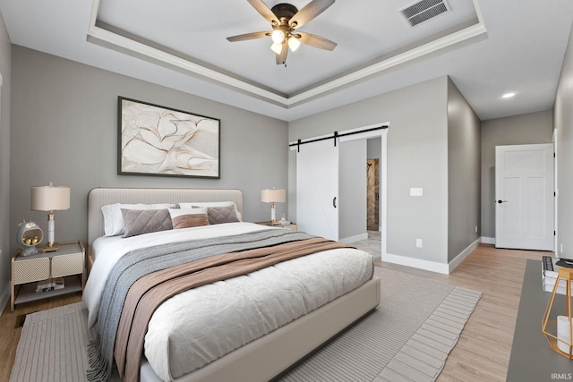 bedroom with visible vents, light wood-type flooring, a barn door, a raised ceiling, and baseboards