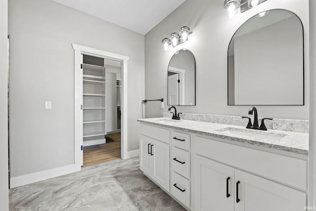 bathroom featuring baseboards, a sink, marble finish floor, and double vanity