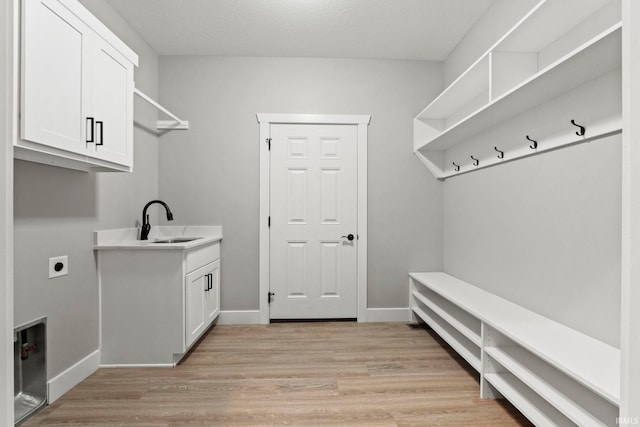 clothes washing area with sink, cabinets, a textured ceiling, hookup for an electric dryer, and light wood-type flooring