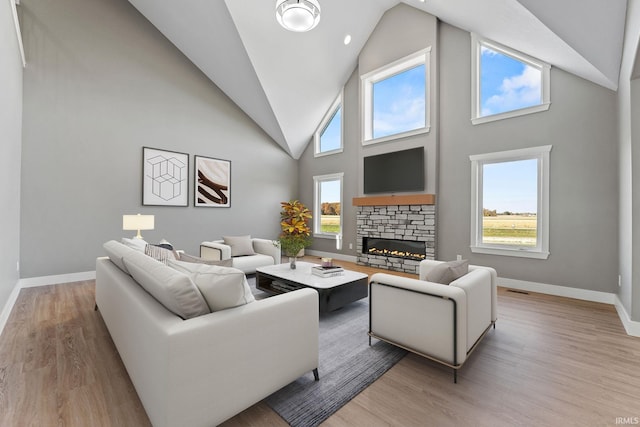 living room featuring a high ceiling, a stone fireplace, and light wood-type flooring