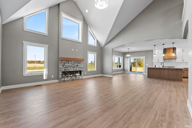 unfurnished living room with plenty of natural light, a towering ceiling, a fireplace, and light hardwood / wood-style floors