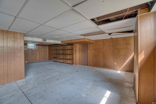 basement with a drop ceiling and wooden walls