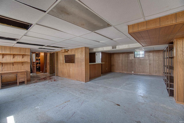 basement featuring wooden walls and a drop ceiling