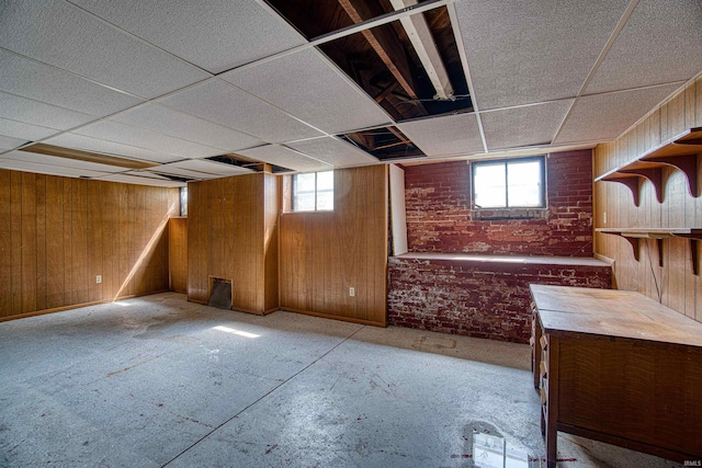 basement with brick wall, a drop ceiling, plenty of natural light, and wood walls