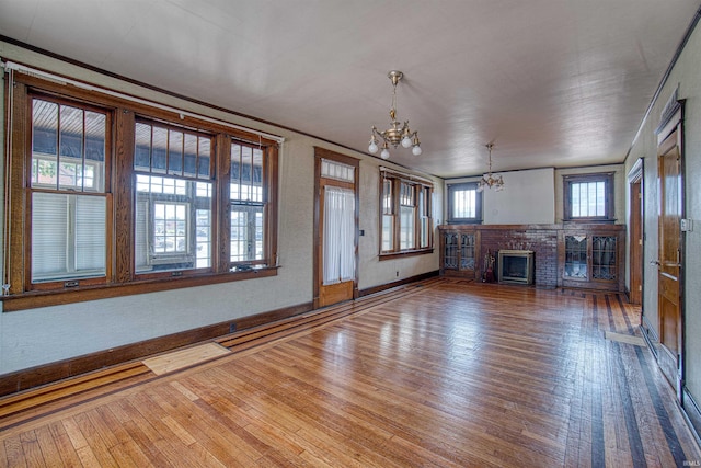 unfurnished living room with a chandelier, wood-type flooring, a brick fireplace, and crown molding