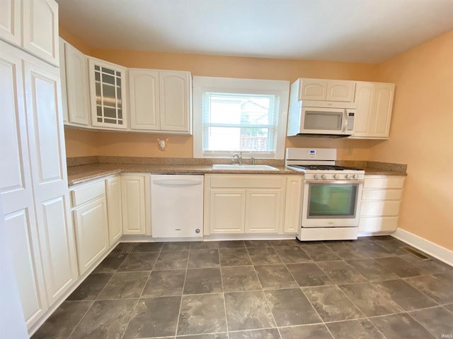 kitchen with white cabinets, dark tile patterned flooring, white appliances, and sink