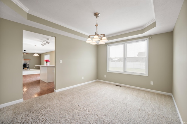 carpeted empty room featuring a raised ceiling, a chandelier, a brick fireplace, and ornamental molding