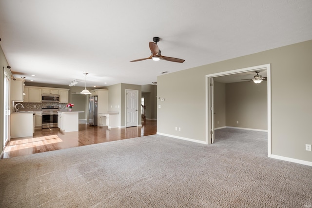 unfurnished living room with light carpet, ceiling fan, and sink