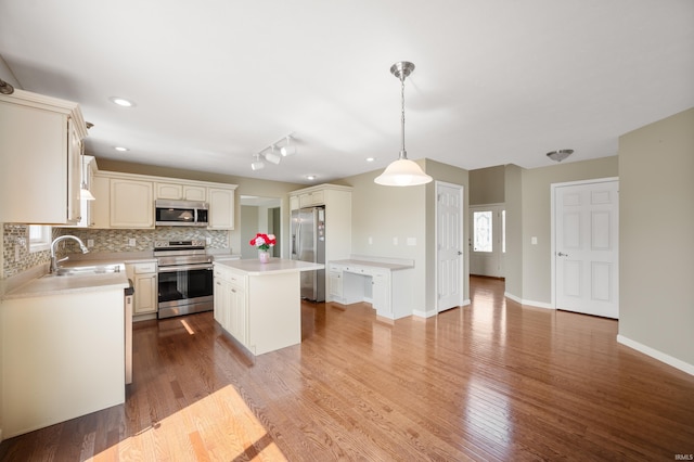 kitchen featuring appliances with stainless steel finishes, decorative backsplash, hanging light fixtures, a kitchen island, and sink