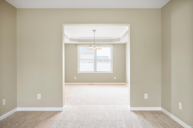 carpeted empty room with a chandelier, ornamental molding, and a raised ceiling