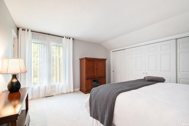 bedroom with vaulted ceiling, light carpet, and a closet